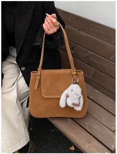 Detail of a brown suede bucket bag with white stitching and a plush rabbit pendant
