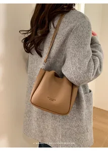 Détail du sac seau en cuir grainé marron avec logo embossé et bandoulière en gros plan