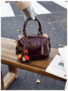 Detail of vintage brown Boston bag with leaf pendant on a park bench with autumn leaves