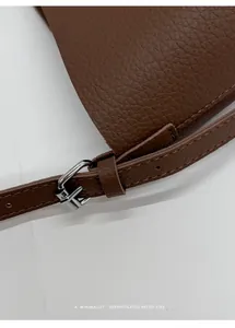 Detail of lychee pattern leather and silver metal buckle on brown shoulder bag