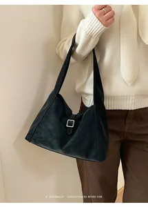 Close-up of a minimalist black suede shoulder bag with silver metal buckle on a model