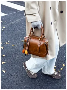 Close-up of caramel Boston bag with leaf charms held by a person in a stylish trench coat