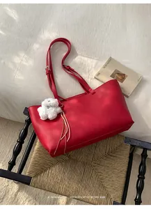 Detail of red PU leather tote bag with white plush dog charm on a woven stool