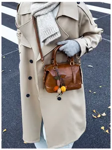 Brown leather Boston bag with leaf pendant charm worn with a beige trench coat