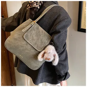 Detail view of a vintage grey-green bucket bag with adjustable strap and plush bunny charm
