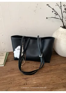 Detail of black pebbled leather tote bag on wooden desk with white puppy charm accent