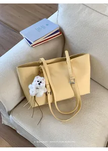 Detail of cream yellow PU leather tote bag with white plush dog charm on sofa