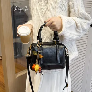 Chic black glossy Boston bag with leaf charms and gold hardware held by a model