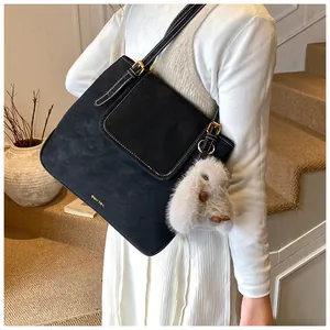 Detail of black suede bucket bag with white contrast stitching and plush rabbit charm