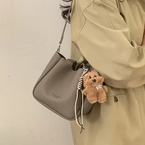Sac seau en cuir gris avec charm ours porté par un mannequin en trench-coat kaki