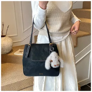 Close-up of matte black bucket bag with a cute white plush bunny charm and metal buckle