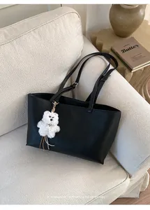 Close-up of black leather tote bag with plush bear charm on a soft fabric sofa