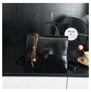 Detail der schwarzen glänzenden PU-Lederhandtasche mit Metallschnalle und Glockenanhänger