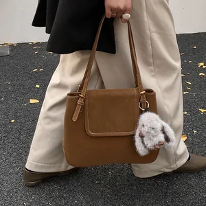 Brown suede bucket shoulder bag with plush rabbit charm and elegant contrast stitching