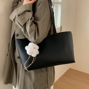 Minimalist large black PU leather tote bag with floral charm shown on model's shoulder