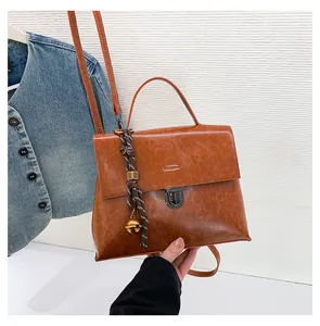 Details der braunen Vintage-Handtasche mit Metallschnalle und dekorativem Glockenanhänger