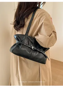 Détail du sac en cuir noir avec boucle argentée porté sur un trench-coat de couleur kaki