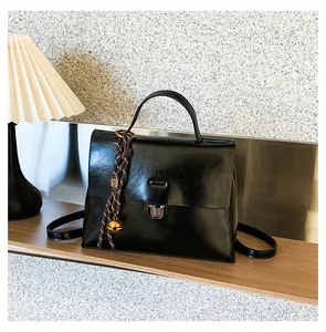Detailansicht einer schwarzen glänzenden Kuriertasche mit Schloss und Taschenanhänger