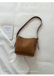 Vue détaillée de dessus d'un sac seau en daim marron avec bandoulière sur tissu