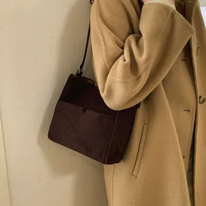 Sac seau en daim marron avec poche décorative en V porté sur un manteau en laine camel