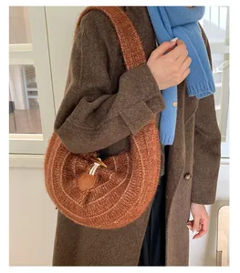 Detail of orange knitted crescent bag with wooden toggle buckle on a brown coat