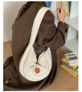 Detailed view of white knitted shoulder bag with a dark horn buckle and leather patch