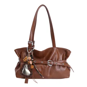 Sac bandoulière en cuir ciré marron avec breloques décoratives sur fond blanc épuré