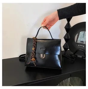 Detail einer schwarzen glänzenden Handtasche mit silbernem Drehschloss und Seilanhänger