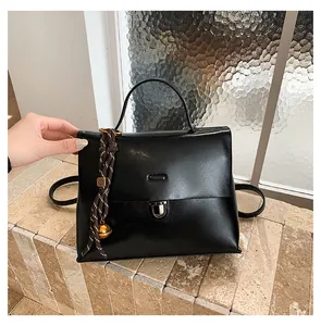 Details einer mattschwarzen Ledertasche mit geflochtenem Anhänger auf Steingrund