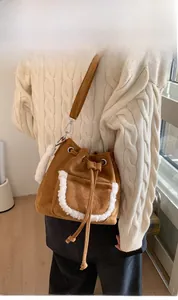 Detail of brown suede bucket bag with plush trim and drawstring closure on white sweater