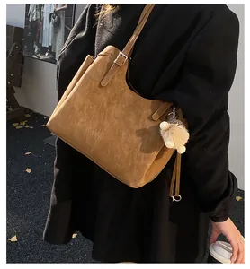 Detail of a brown suede tote bag featuring a side buckle and a white plush ball charm