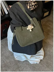 Deep green faux leather tote bag with plush charm shown in a cozy studio setting