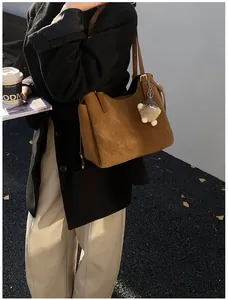Detail of dark brown tote bag with matte texture, side pocket, and plush ball charm