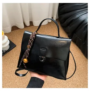 Detail der glänzenden schwarzen Ledertasche mit Logo-Metallperle und goldenem Glockenanhänger
