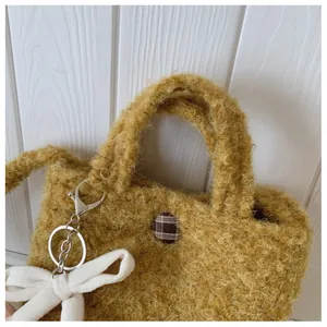 Detail der senfgelben Plüsch-Beuteltasche mit Karoknopf und weißem Schleifenanhänger