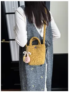 Detail der ingwerfarbenen Plüsch-Mini-Beuteltasche mit Anhänger auf grauem Outfit