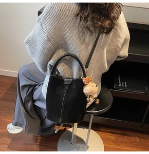 Detail of black suede bucket bag featuring contrast stitching and a cute bear charm