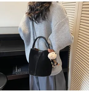 Detail of black suede bucket bag with contrast stitching and a cute teddy bear charm