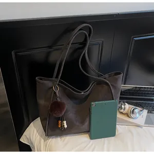 Détail du sac fourre-tout en daim gris anthracite avec pendentif peluche sur lit blanc