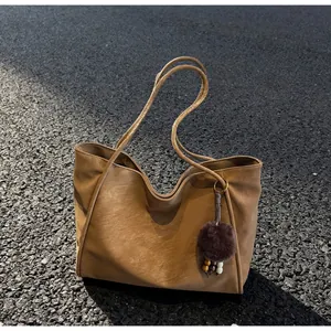 Détail d'un grand sac cabas en suédine marron caramel avec un charm pompon en peluche