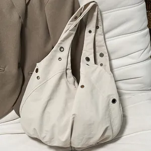 Minimalist beige crescent shoulder bag with silver eyelets and textured fabric