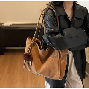 Détail d'un grand sac cabas en daim marron avec un pendentif en peluche et perles colorées
