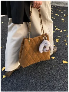 Detail van bruine gewatteerde tas met gouden ketting en pluche konijnenhanger-accent