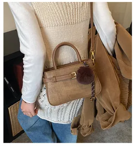 Detail of vintage brown bucket bag with woven texture, metal buckle and plush pom-pom charm