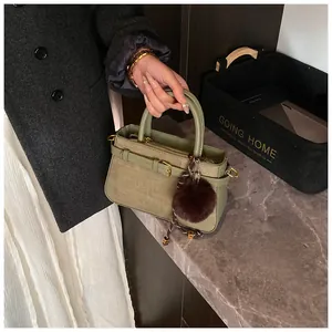 Detail of green woven bucket bag with smooth leather handle and plush brown pompom charm