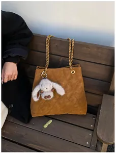 Detail van gewatteerde suède tas met gouden ketting en pluchen konijnenhangertje