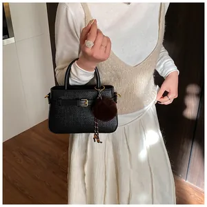 Detail of black woven texture handbag with gold buckle and brown faux fur pompom charm