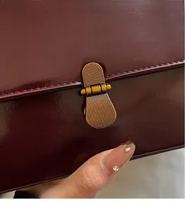 Macro detail of wine red glossy leather bag featuring a vintage 3D gold metal buckle