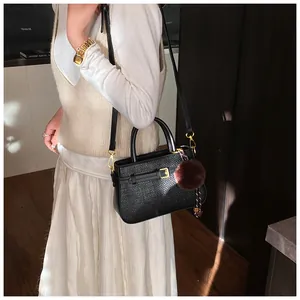 Detail of black textured bucket bag featuring gold buckle and brown fur pompom accessory