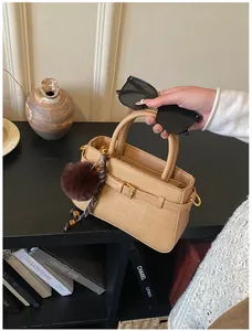 Close-up of beige textured handbag with decorative buckle and plush brown pompom charm